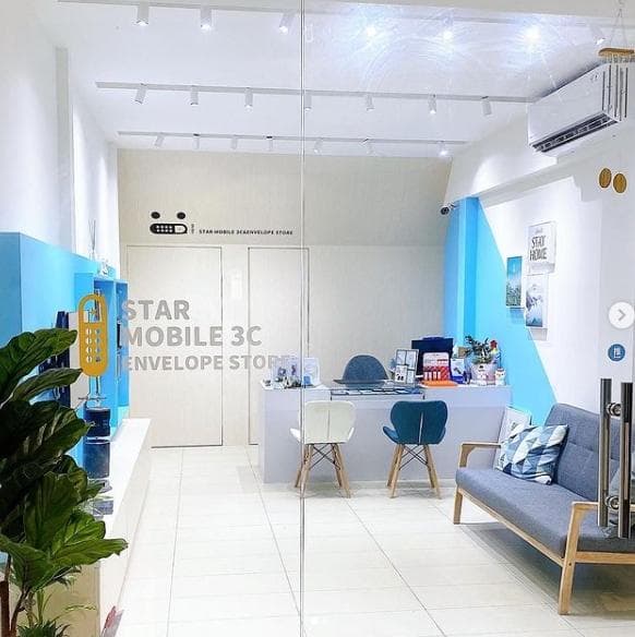 這張「手機店」的照片是一個明亮的店面,有白色和藍色的牆壁,以及木質地板。牆上有一個「STAR MOBILE 3C ENVELOPE STORE」的招牌。店裡有兩張椅子和一個沙發,以及一個櫃檯,方便顧客諮詢。