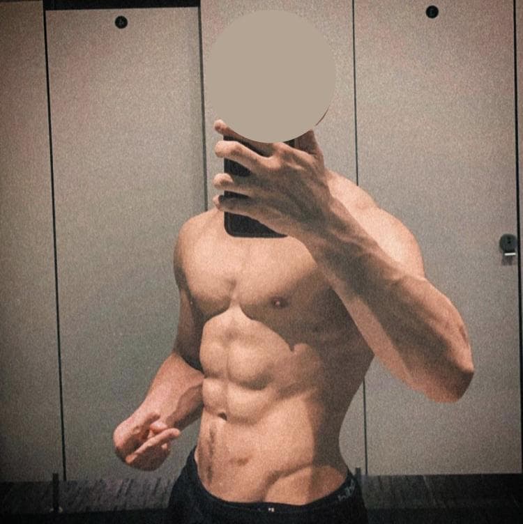 這張「健身房自拍」的照片是一個男性在鏡子前展示他的肌肉,他穿著短褲,舉起手機拍照,看起來非常自信。