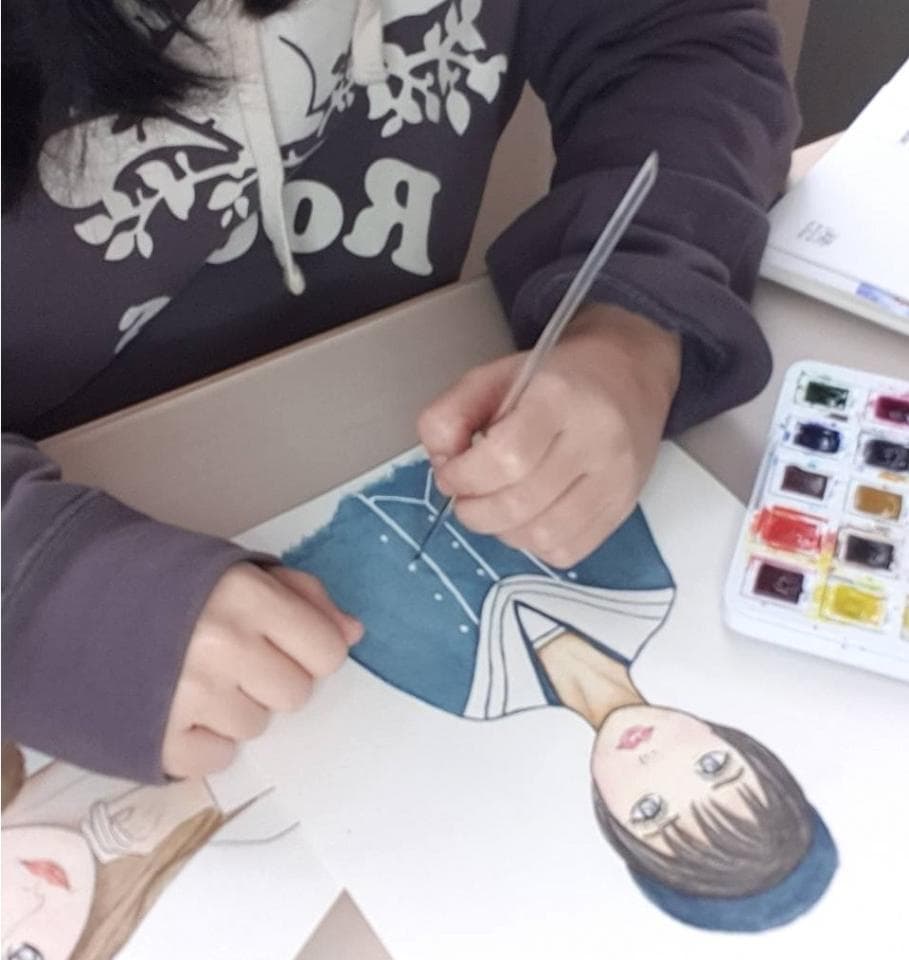 這張照片是一名女子正在畫畫,她用畫筆在紙上細心地描繪著一個女孩的肖像,畫紙上已經有了一些線條和色彩,女孩的面部表情看起來很可愛。