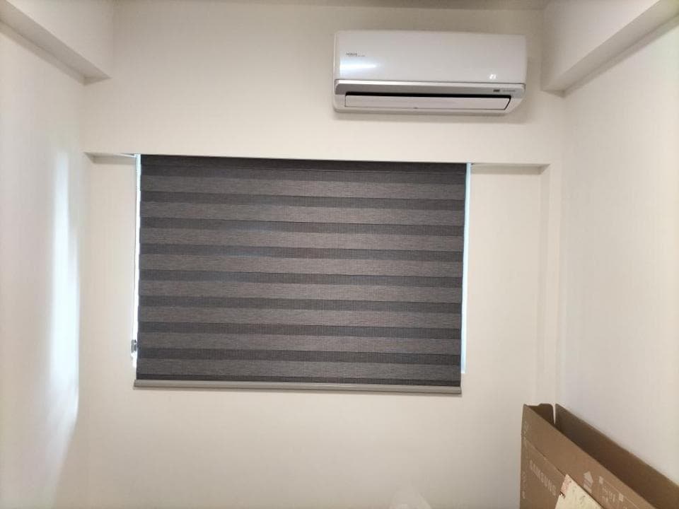 1) 這是一張室內照片,照片中顯示一個房間,房間裡有一台冷氣機,窗戶上裝有百葉窗簾,以及一個放在牆邊的紙箱