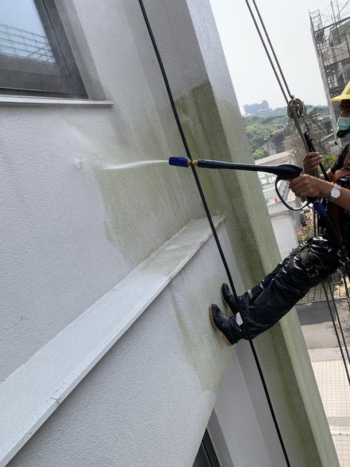 1) 照片描述: 一位身穿黑色工作服的工人站在一栋建筑物的外墙上,正在用高压水枪清洗墙壁