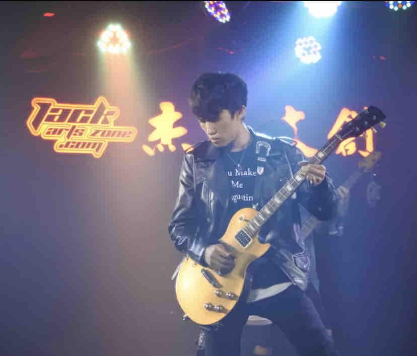 這張照片是一個年輕人正在彈奏電吉他。他身穿黑色皮衣,戴著黑色帽子,專注地演奏著音樂。他的姿勢和表情都充滿了熱情和活力。