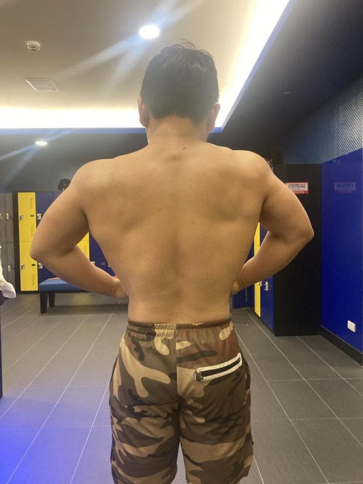 這張照片是一個男性站在更衣室的鏡子前,他穿著迷彩短褲,背對著鏡頭。