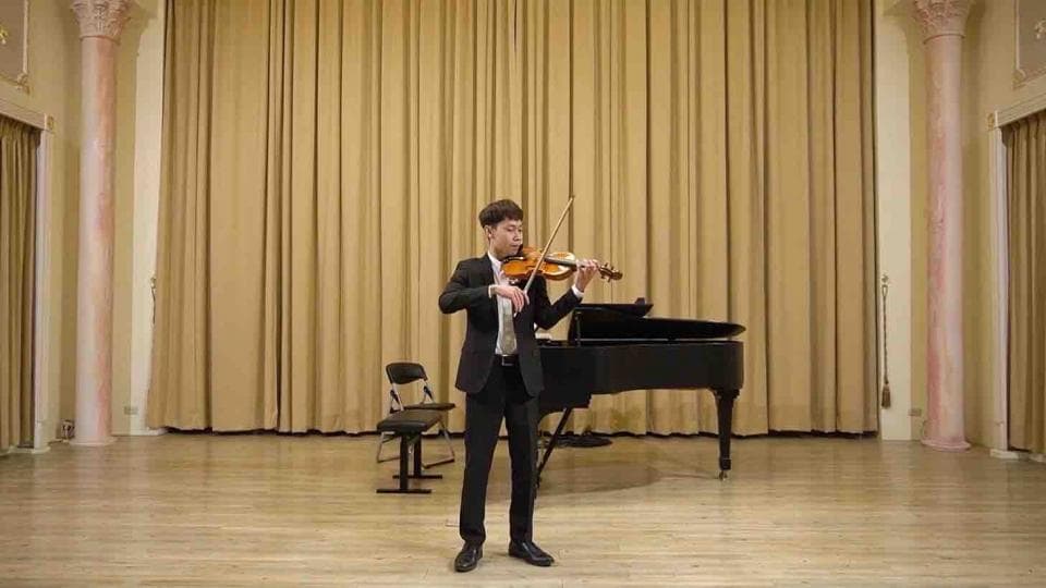 這張照片是一個年輕的小提琴手正在演奏。他穿著黑色西裝,神情專注,右手拉弓,左手按弦,正在演奏一首動聽的樂曲。