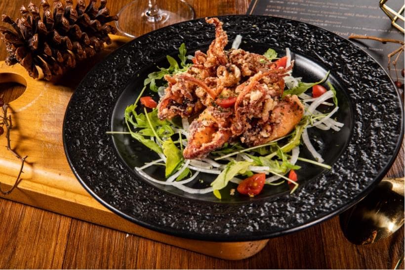 這張「炸魷魚」的照片是放在黑色盤子上的,魷魚被炸得酥脆,配上綠色的蔬菜和一些紅色的番茄。