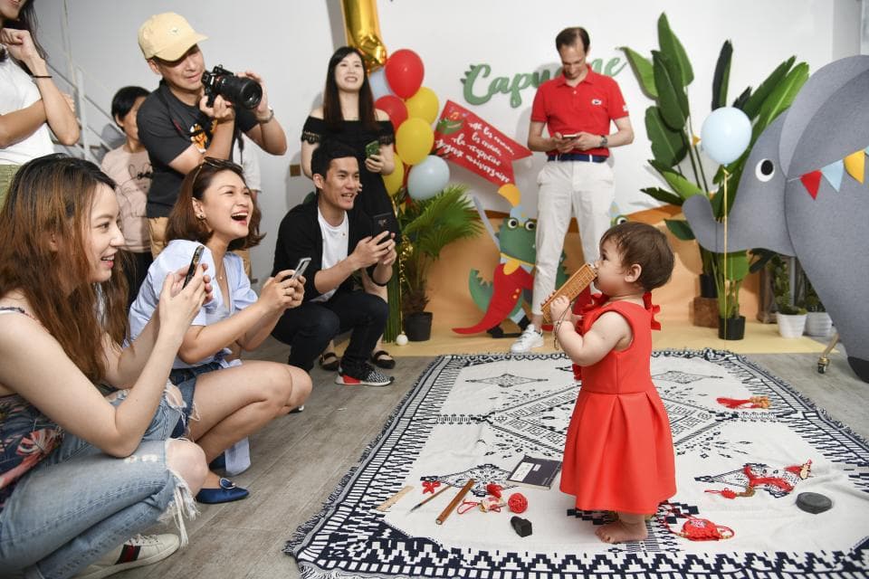 這張照片是一個兒童派對,一個穿著紅色連衣裙的小女孩站在地毯上,她正看著鏡頭微笑。