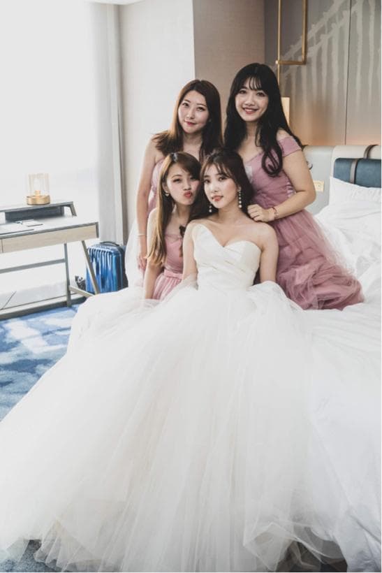這張「婚禮」的照片是新娘和三個伴娘在酒店房間裡。新娘穿著白色的婚紗,伴娘穿著粉色的禮服。她們看起來都很開心和興奮。