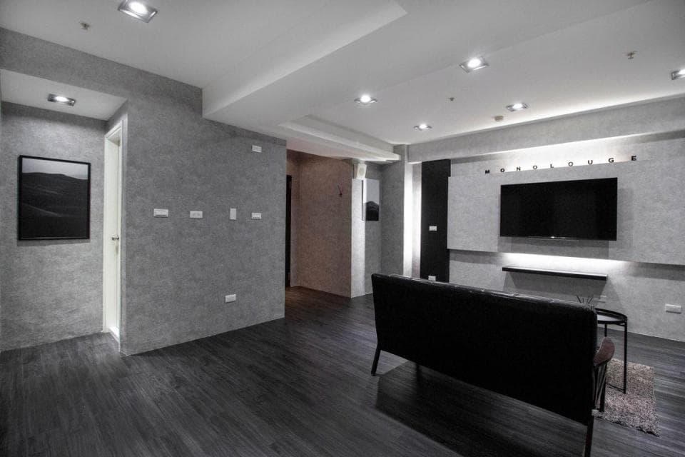 1) 照片顯示一個現代化的客廳,牆壁刷了灰色的油漆,地板是深灰色的木板,客廳的中心擺放著一個黑色的沙發,電視牆上裝置著一臺黑色的電視,以及一個黑色的電視櫃