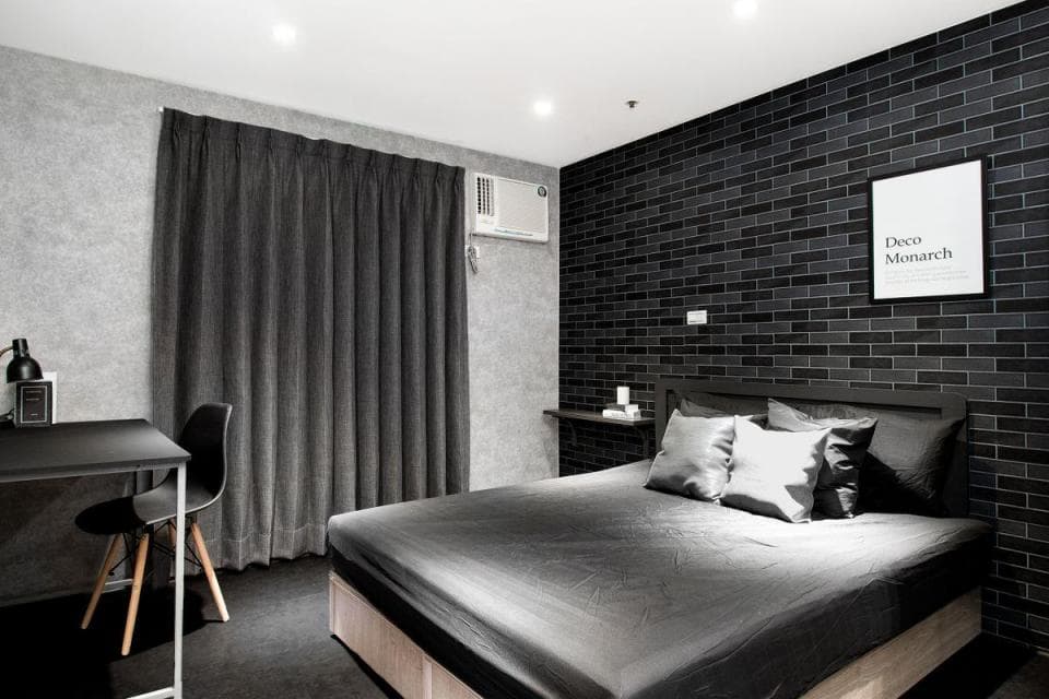 1) 照片顯示一個現代臥室,房間以灰色和黑色裝飾,牆壁以黑色磚塊為主,並配有灰色窗簾