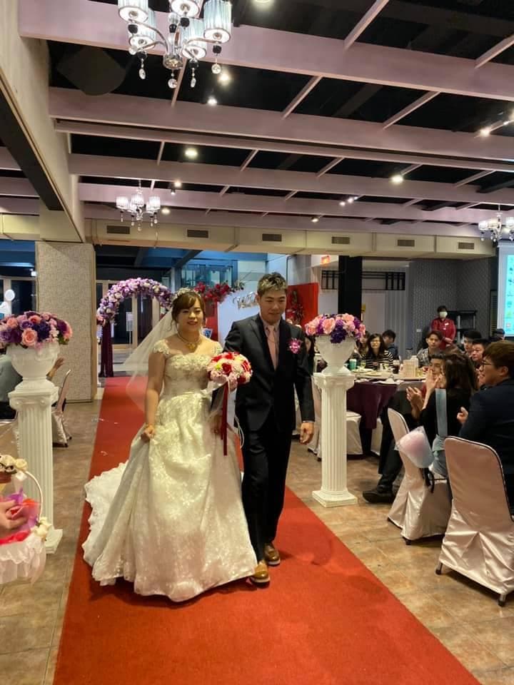 這張「婚禮」的照片是新郎新娘在紅毯上走,新娘穿著白色的婚紗,新郎穿著西裝,他們手牽手,看起來很幸福。