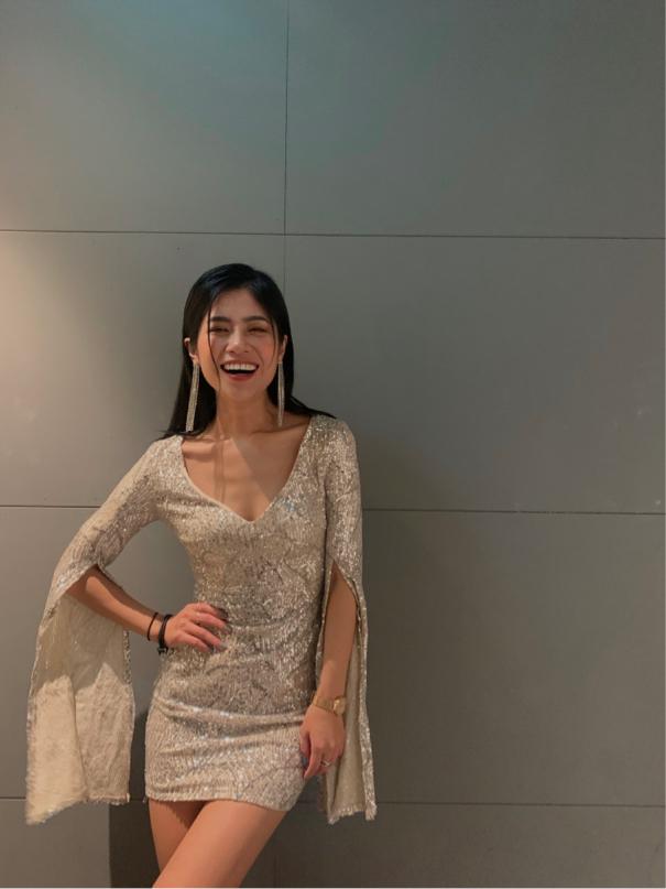 這張照片是一個穿著金色亮片連衣裙的年輕女子,她對著鏡頭微笑,顯得非常開心。