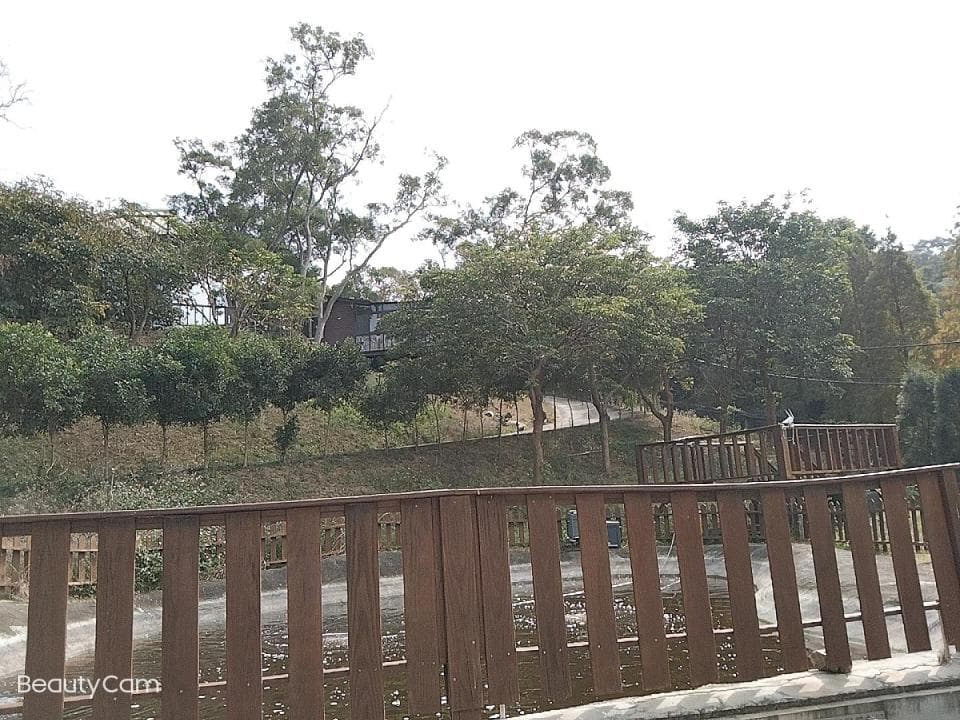 1) 這張照片顯示了一個木質欄杆,後面是一片樹林和房屋