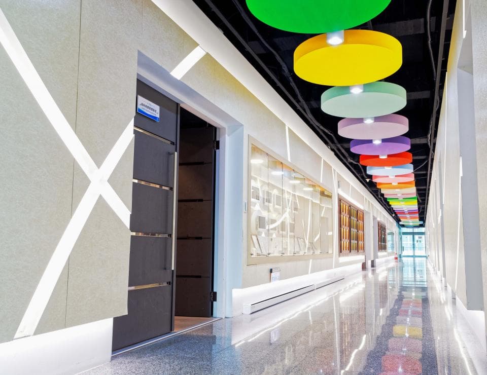 這張「走廊」的照片是一個明亮而現代的空間,牆壁上有交叉的白色線條,天花板上裝飾著一排彩色圓形燈。