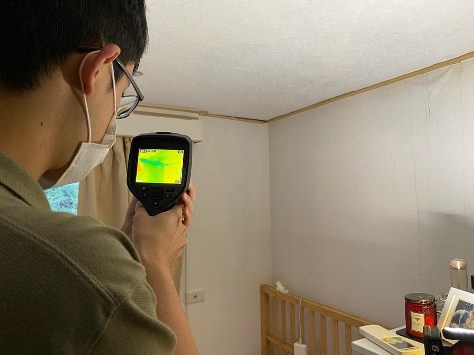 1) 照片顯示一名戴著口罩的男子,拿著熱像儀檢查房間的牆壁