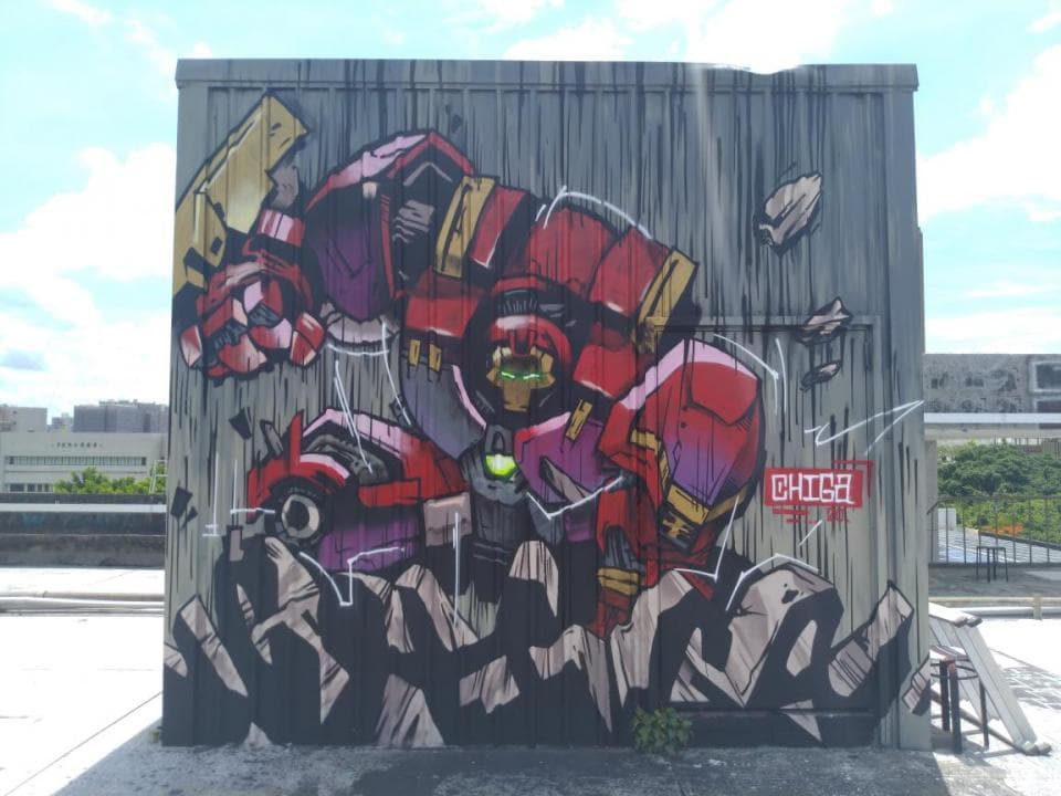這張塗鴉的照片是一個巨大的機器人,他站在建築物的一面牆上,手上拿著一把巨大的武器。機器人的身體是由紅色和紫色組成,他的眼睛看起來很兇狠。
