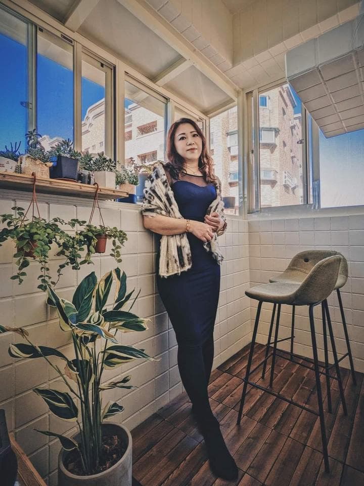 這張「女人站在房間裡,穿著黑色連衣裙,背景是窗戶和植物」的照片是。