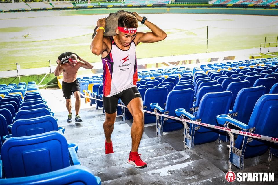 這張照片是一名男子在障礙賽中爬梯子,他手上拿著一塊石頭,背景是觀眾席。