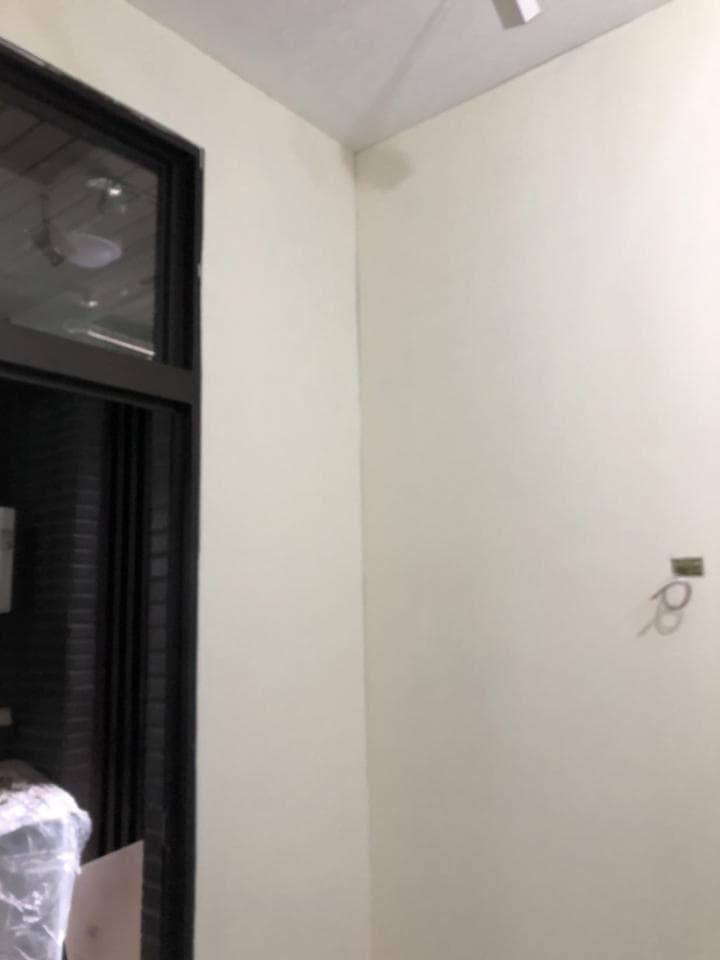 1) 照片顯示一個房間的角落,牆壁是白色的,角落有一扇黑色的門,天花板是白色的,牆壁上有一個小洞