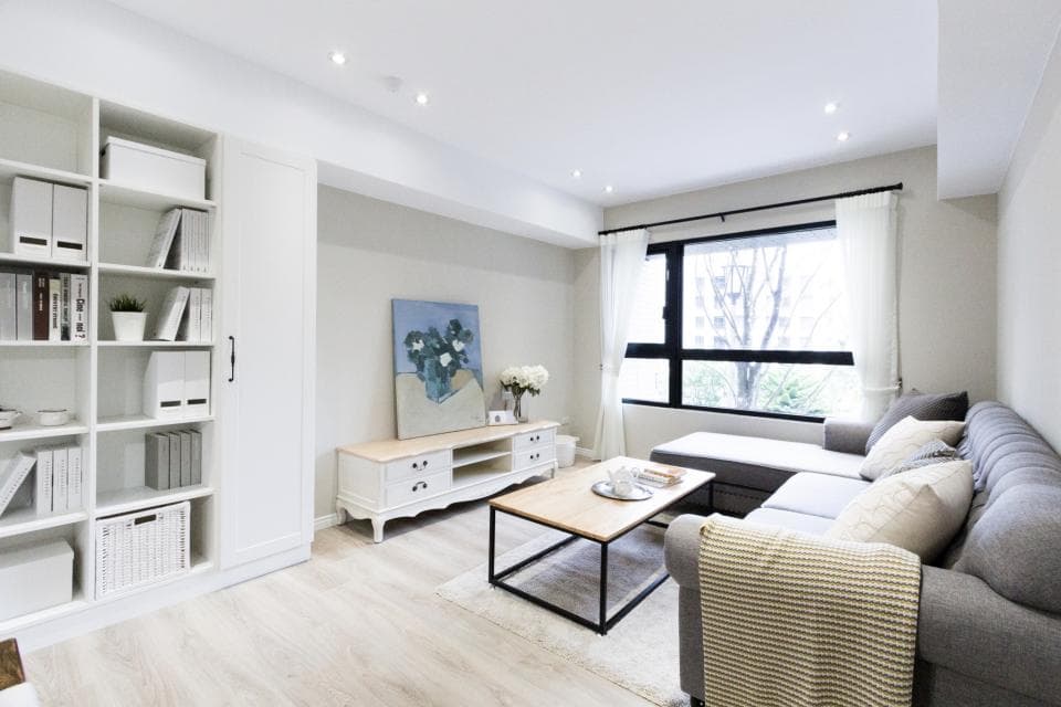 這張「現代客廳」的照片是:一個白色和灰色的客廳,有一個大大的落地窗,旁邊有一個舒適的沙發,還有白色櫃子,裝飾著畫和植物。