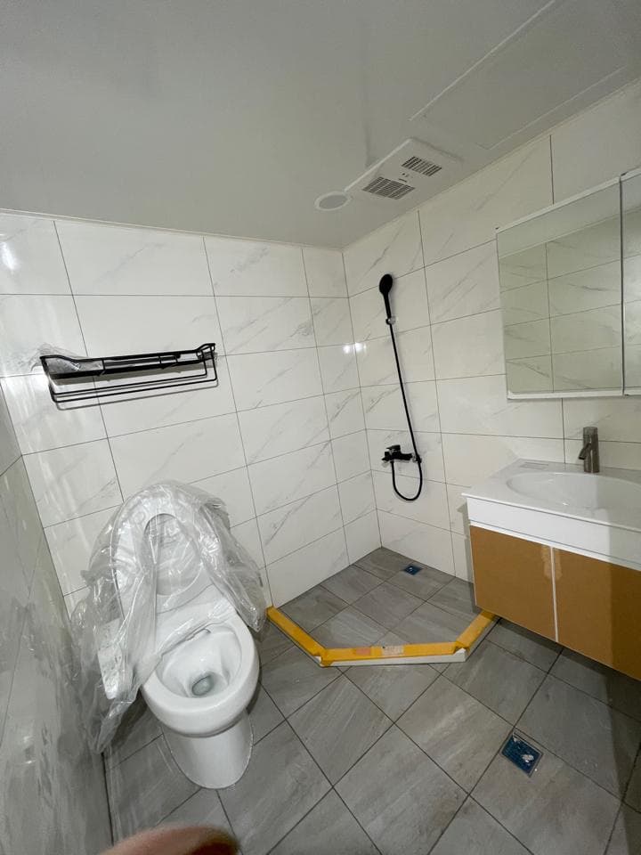 這張照片是一間正在裝修的浴室,重點是地上鋪設的灰色瓷磚,以及角落處尚未完成的黃色防水層。