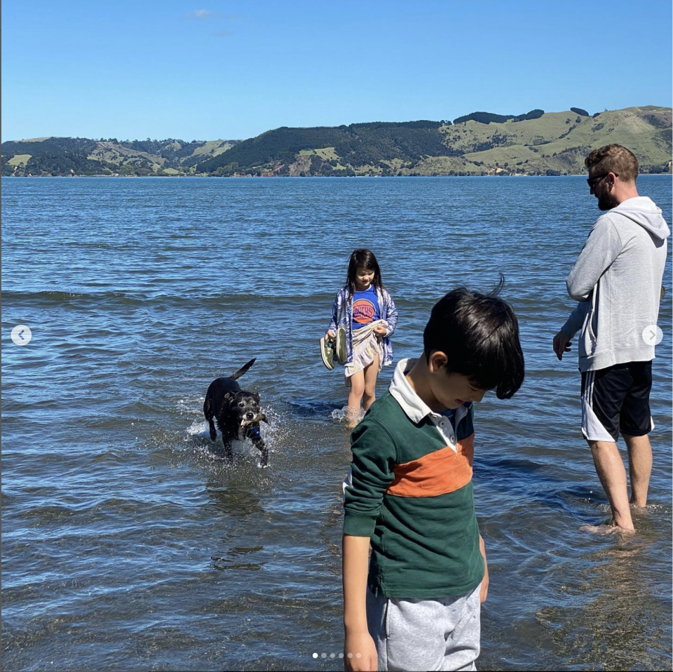 1) 照片中有一位成年男性和兩位兒童站在海灘上,一個女孩正在水中行走,一個男孩正在水中玩耍,一隻黑色的狗狗在水中游動