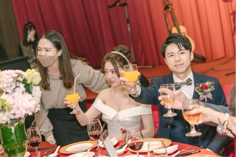 這張照片是一對新人在婚禮上舉杯慶祝,新娘穿著美麗的婚紗,新郎則穿著西裝,他們都露出了幸福的笑容,畫面充滿了喜悅和溫馨。