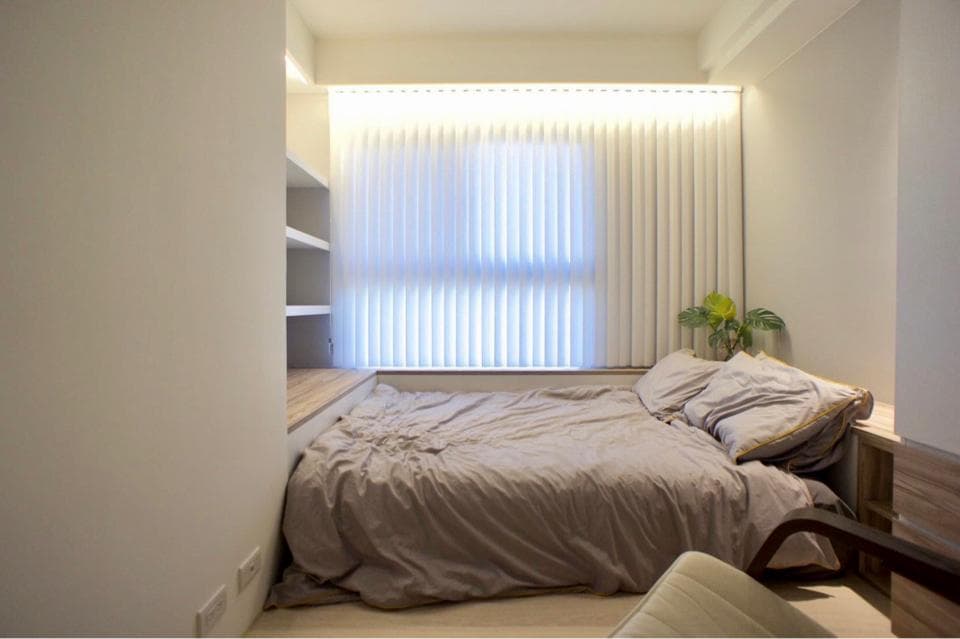 1) 這張照片展示一個簡約的臥室,房間裡有一張床,床上鋪著淺色被子,牆上裝著百葉窗,以及木製的書架和床頭櫃