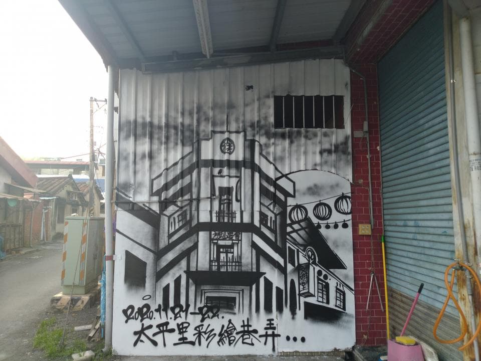 這張「牆壁上的塗鴉」的照片是,一幅以黑色線條描繪的建築物圖案,牆上還寫著「大平重製魚糕香」,牆壁的右邊是藍色的鐵門。