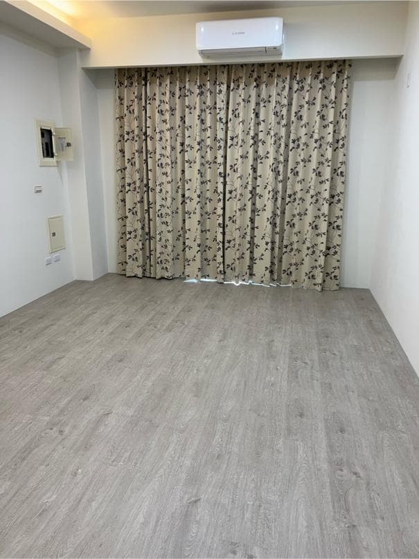 這張照片是一個有著木紋地板的空房間,房間裡有著灰色的窗簾,非常簡單舒適。