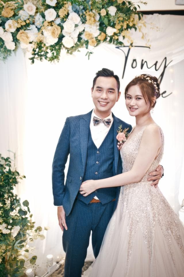 這張「婚禮」的照片是一對新人,新郎穿著藍色西裝,新娘穿著白色婚紗,兩人互相依偎,背景是白色的花拱門。