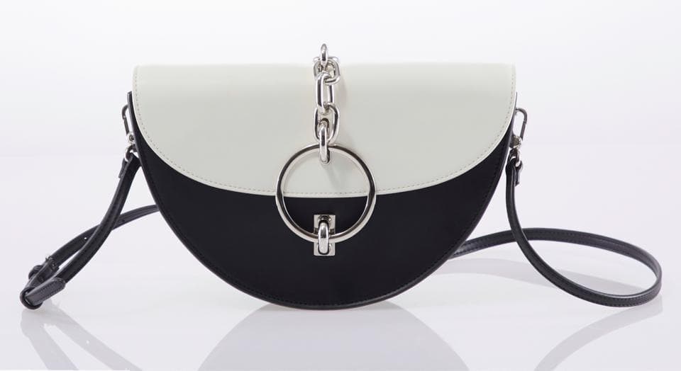 這張照片是一隻黑白色的半圓形手提包,包上有一個銀色的圓形金屬裝飾,裝飾上連著一條銀色的鏈子,整體設計簡約時尚。