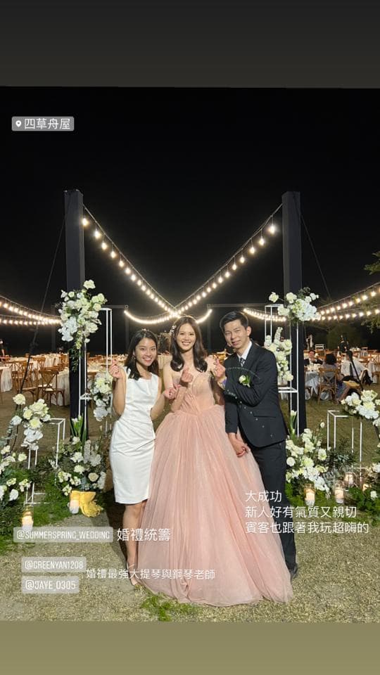 這張照片是一對新人和他們的伴娘,在戶外婚禮的現場,新娘穿著粉色的婚紗,伴娘穿著白色的禮服。他們站在拱門前,背景是佈置精美的婚禮場地。