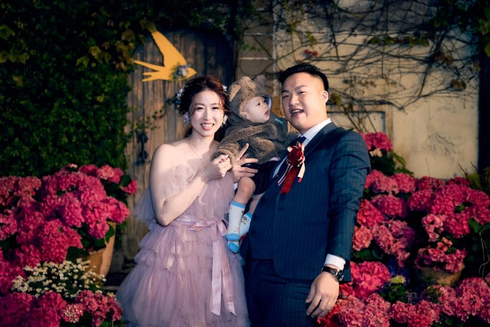 這張「婚禮」的照片是一對新婚夫婦和他們的小孩在戶外花園中拍的照片,新郎穿著西裝,新娘穿著婚紗,他們的小孩穿著可愛的衣服。