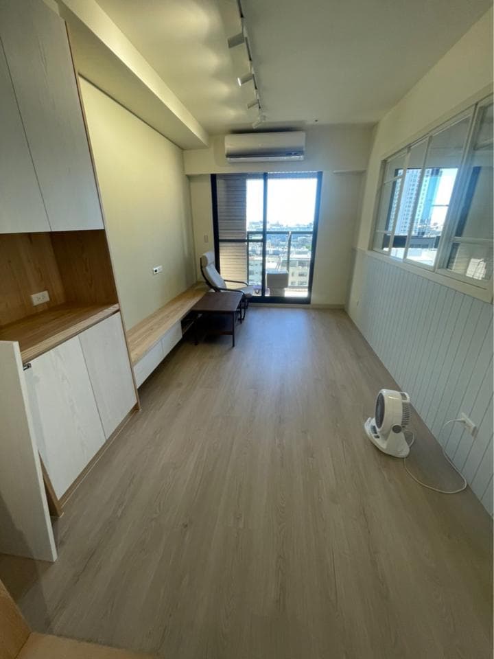 1) 照片顯示一個裝潢好的客廳,客廳地板是木質地板,旁邊有一排白色櫃子,客廳右側有一扇落地窗,窗戶外可以看見遠處的風景,客廳中央有一個小桌子和一個椅子,客廳右邊地板上有台電風扇