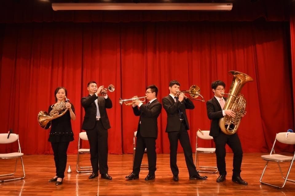 這張照片是五個音樂家在舞臺上表演,其中一位吹著法國號,一位吹著小號,一位吹著長號,一位吹著大號,一位吹著法國號。他們都穿著正式的服裝,看起來很專業。