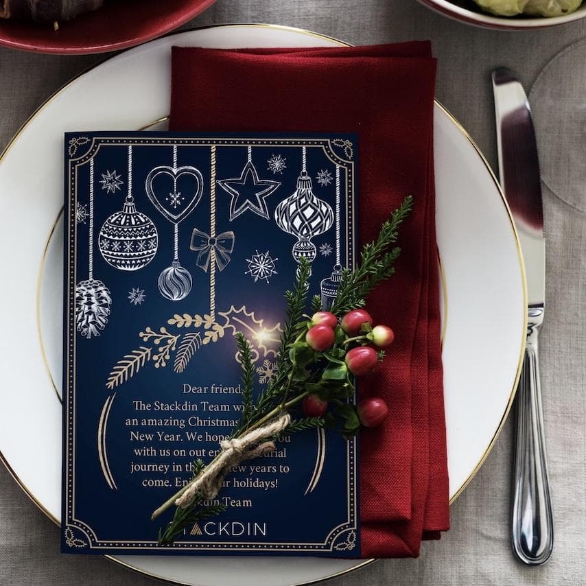 這張「聖誕節餐桌」的照片是一張藍色卡片,上面有金色的聖誕裝飾,旁邊放著一株綠色植物和一些紅色的漿果。卡片上有一段文字,祝福大家聖誕快樂和新年快樂。