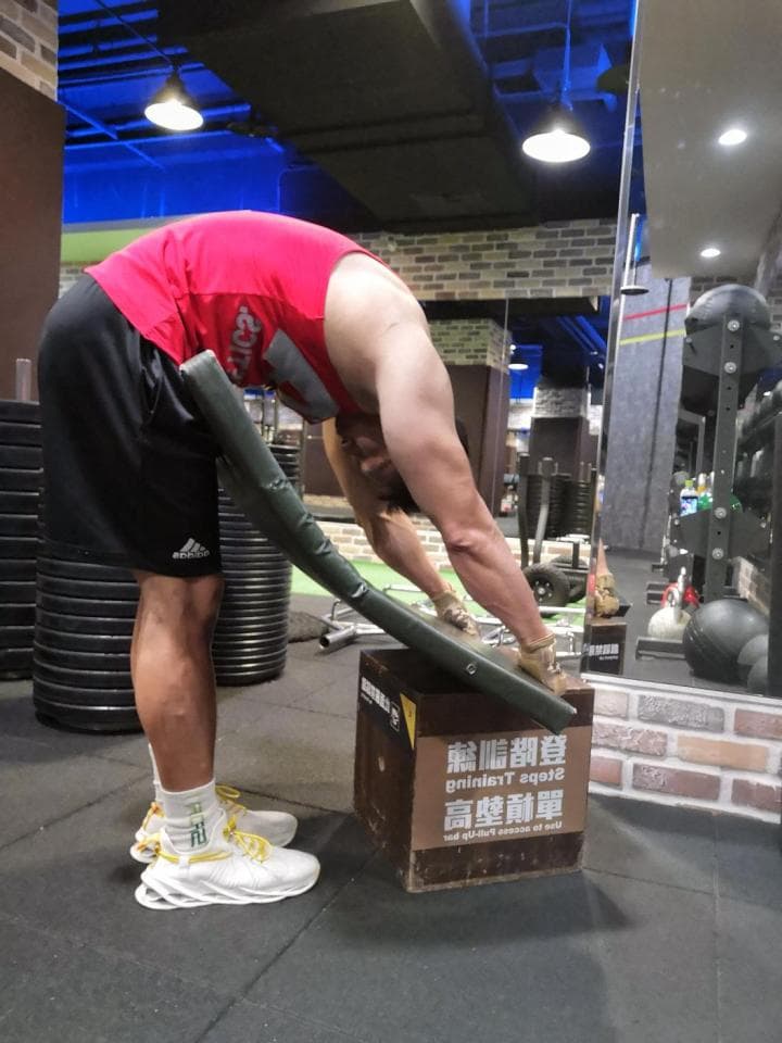 這張照片是一個男人在健身房做伸展運動,他正將身體彎曲到一個木箱上,看起來很吃力。