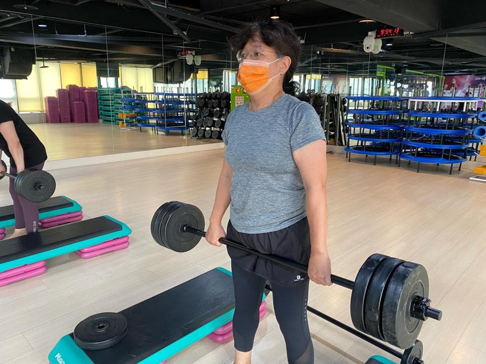 這張照片是一名戴著口罩的女子在健身房舉重,她正在做深蹲舉重訓練,看起來很認真專注。