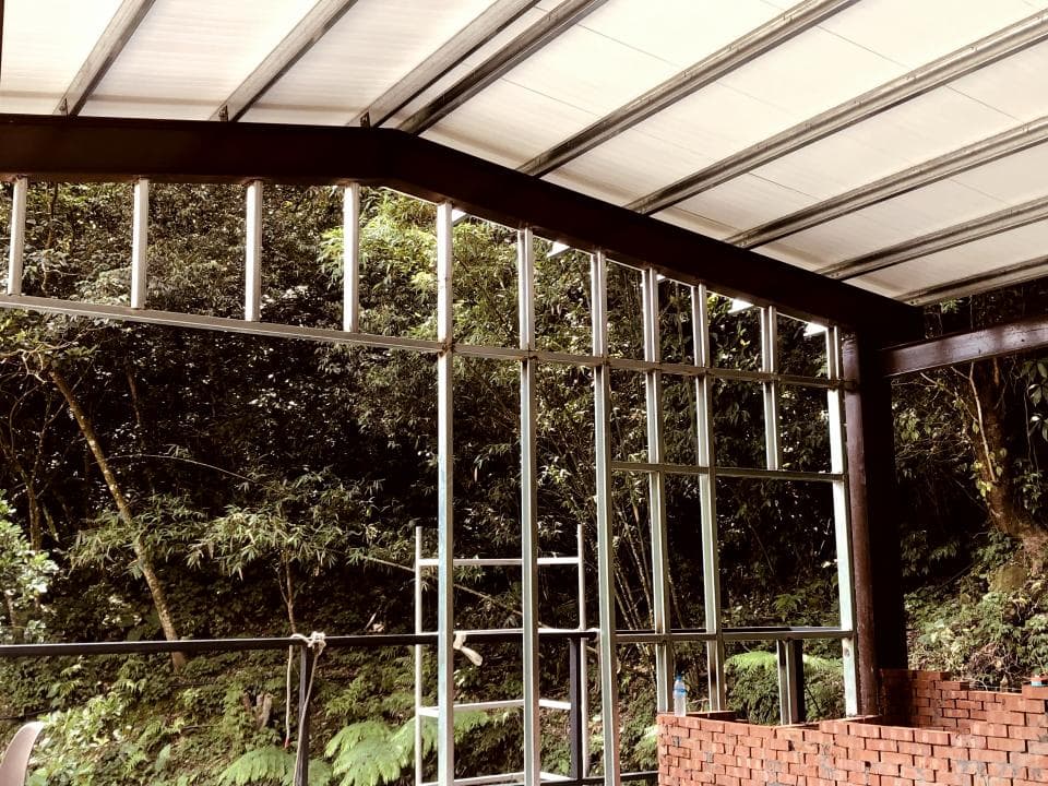 1) 照片顯示一個建築物正在施工的過程,建築物有一層白色金屬屋頂,有橫樑支撐,屋頂下方是鐵製的窗戶,正在建造中