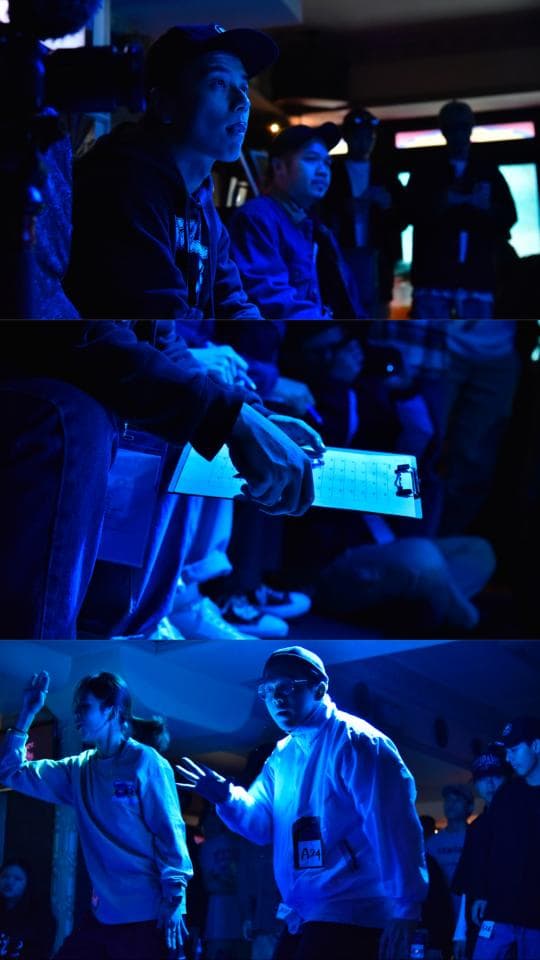 這張照片是一群人在一個昏暗的房間裡。照片中的最主要部分是站在中間戴著帽子的男子,他正面向著鏡頭,並且穿著白色上衣。他身後的背景是模糊的,而他清晰的輪廓則吸引了觀眾的注意。