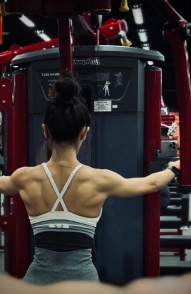 這張照片是一個女生在健身房裡用拉力器做運動。她正在拉著繩索,背部肌肉非常發達。