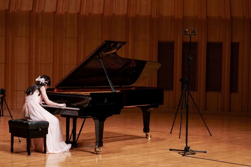 這張「鋼琴演奏」的照片是一個年輕女子坐在鋼琴前演奏,她穿著白色連衣裙,鋼琴是黑色的,背景是木質的牆壁。