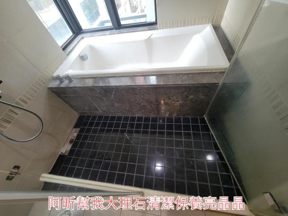 1) 照片顯示了一個浴室,有一個浴缸,浴缸旁邊有一個窗戶,地板是黑色的瓷磚