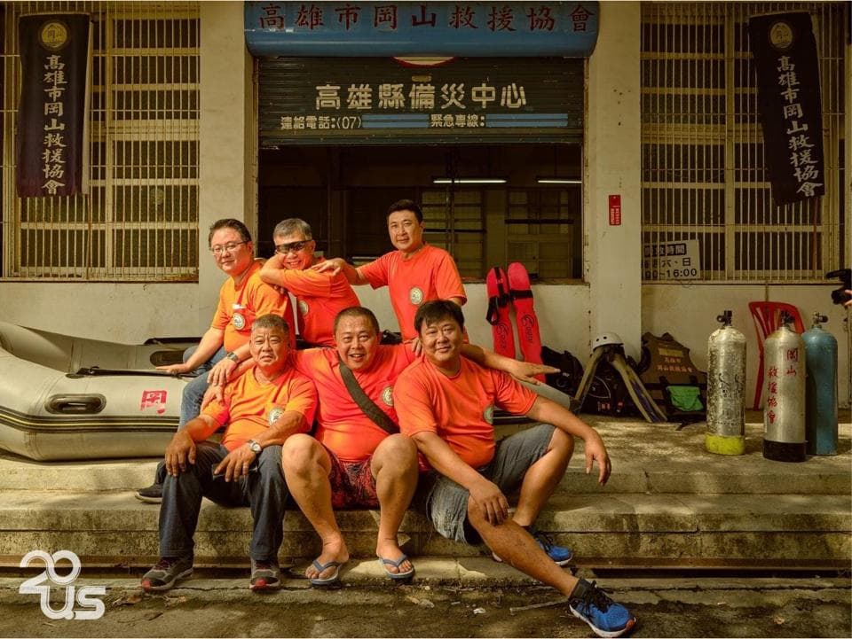 這張「一群男人站在建築物前,他們都穿著橘色的衣服,有人在笑,有些人則在擺出姿勢拍照。」的照片是。