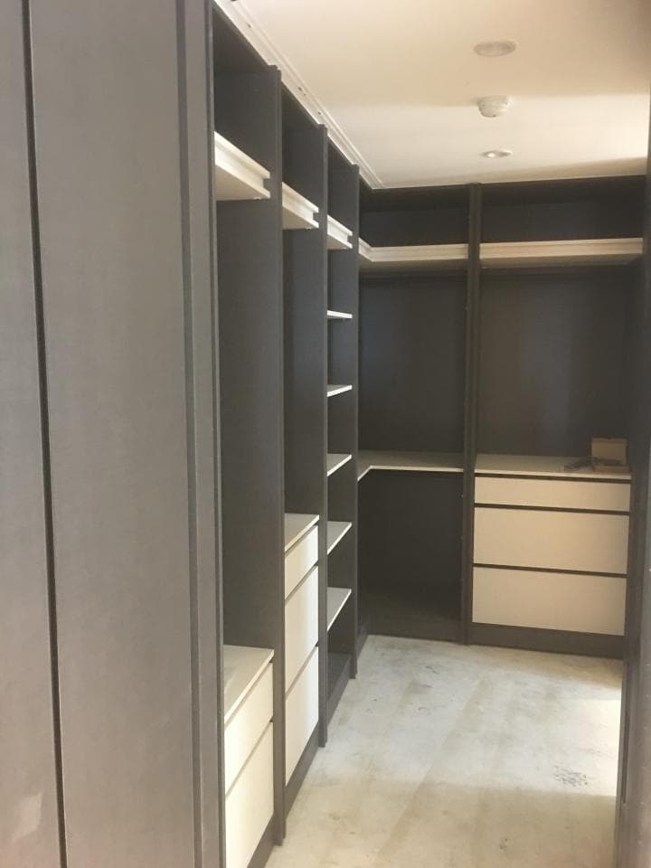 這張照片是一間現代化的衣帽間,配有白色抽屜和深色木質框架,可以收納大量衣物。