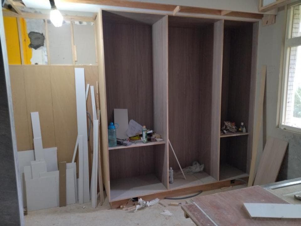 1) 照片顯示一個正在建造中的木櫃,櫃子有四個門,其中兩個門已經安裝完成,另外兩個門還沒安裝,櫃子內部有隔板,櫃子下方有木板,櫃子周圍有一些施工材料,例如木條和油漆