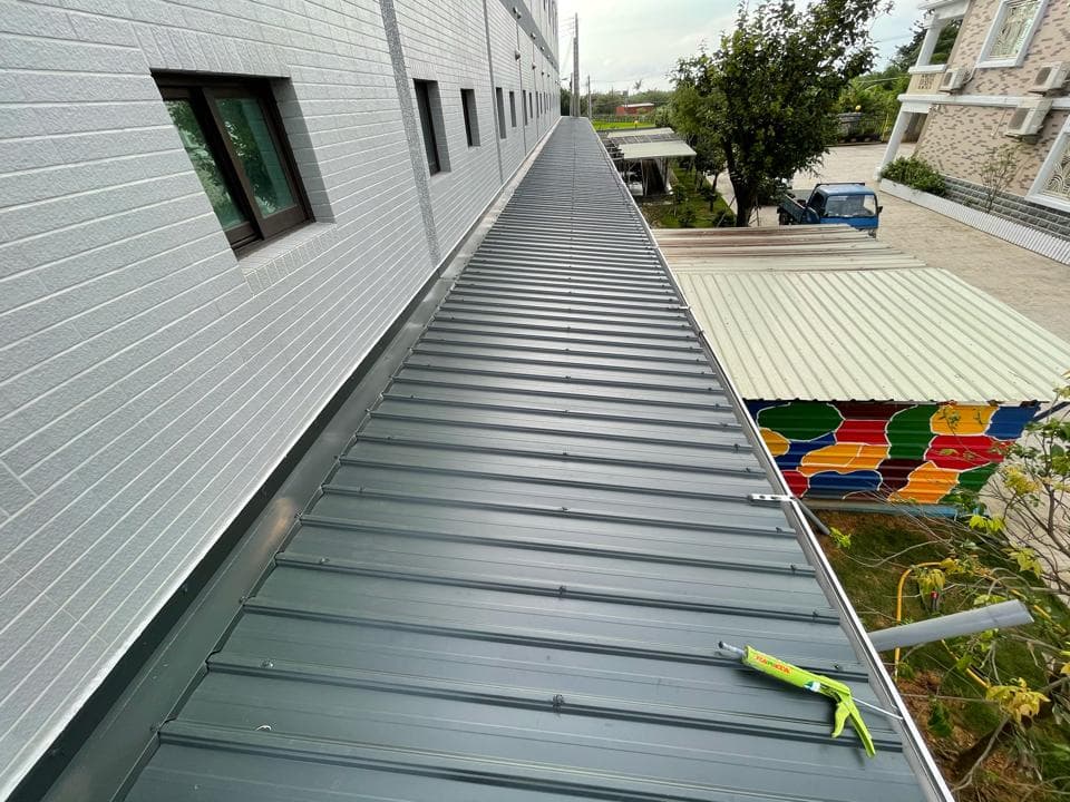 這張「屋頂」的照片是一個帶有灰色金屬瓦的屋頂,上面有一條綠色的防水膠條。