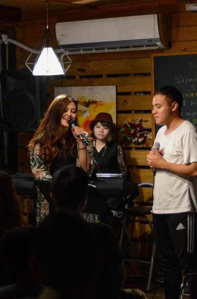 這張「三人在室內唱歌」的照片是,一位女士站在中間,正在唱歌,旁邊有兩位觀眾,其中一位是一位女士,另一位是一位男士。