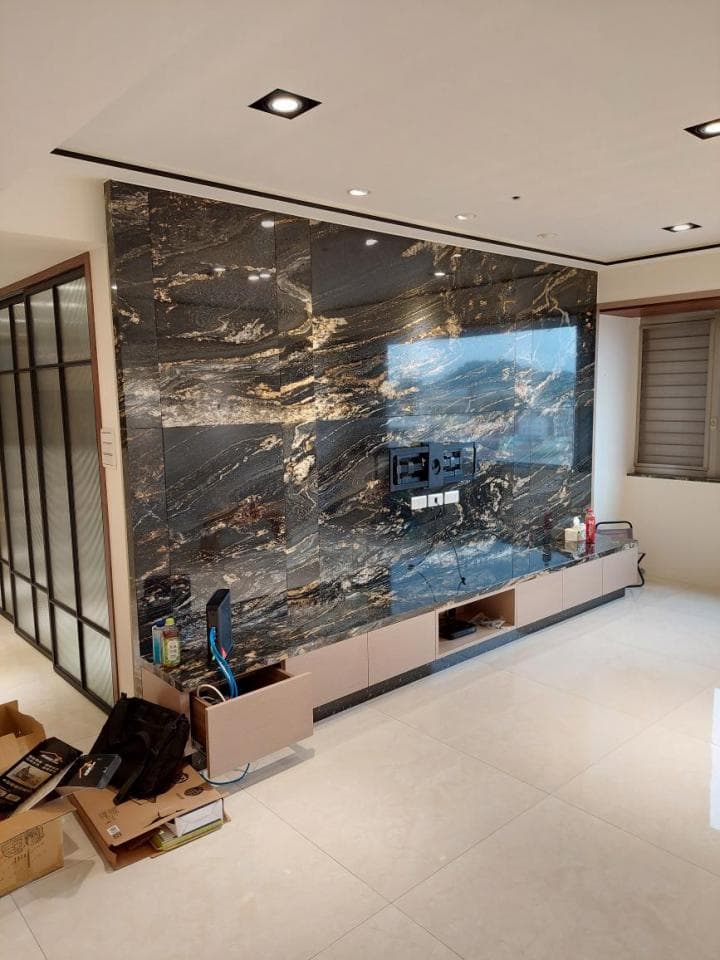 這張照片是一間客廳的電視牆,牆面使用黑色大理石鋪設,帶有金色紋理,顯得高貴奢華。牆上安裝了一台電視,下方是木質電視櫃,整體設計簡潔大方。