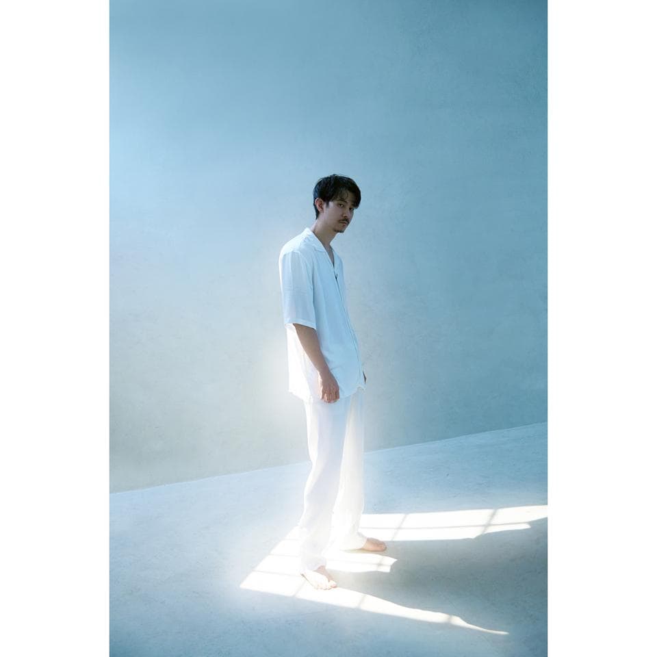 這張「男人穿著白色襯衫和褲子,站在光線充足的白色房間裡」的照片是。